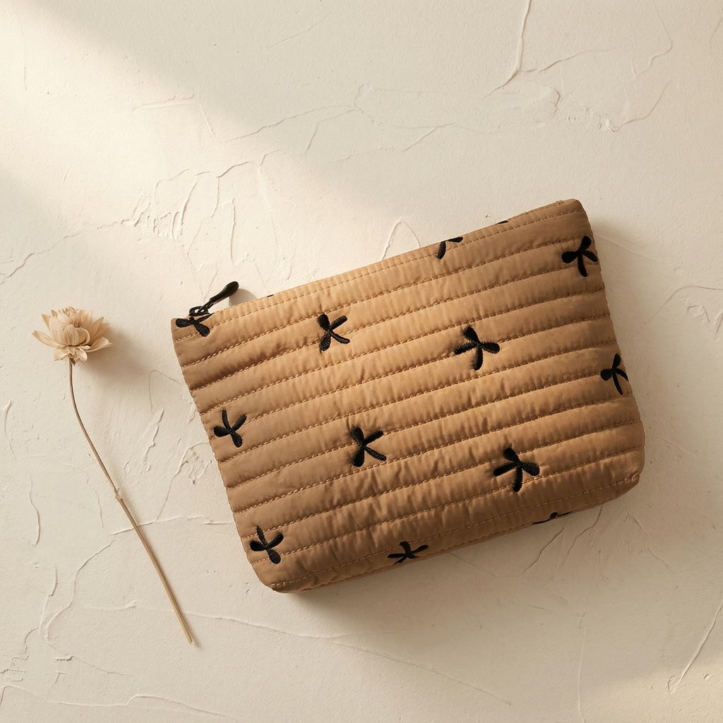 Beige pouch with black floral patterns on a textured beige surface