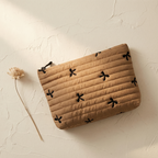 Beige pouch with black floral patterns on a textured beige surface