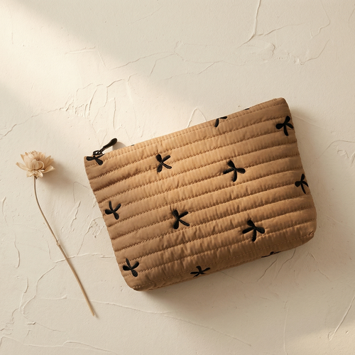 Beige pouch with black floral patterns on a textured beige surface